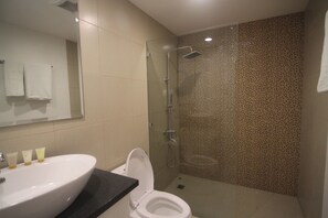 Une salle de bain avec un lavabo blanc, des toilettes, une douche en verre et un mur carrelé à motifs pointillés.