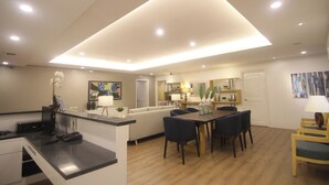 A modern living room with a dining area, a kitchen in the background, and a large ceiling light fixture. - Bryan Condo Suites Makati near Airport (Makati)