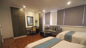 A hotel room with two beds, a desk, a chair, a sofa, and a large window with blinds. - Bryan Condo Suites Makati near Airport (Makati)
