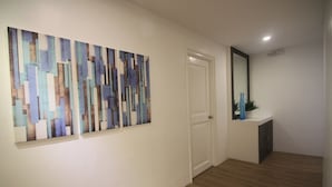 A hallway with a wooden floor, a white door, and a wall with abstract art. - Bryan Condo Suites Makati near Airport (Makati)