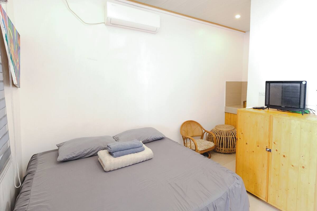A bedroom with a bed, pillows, a wooden wardrobe, a chair, and a television.