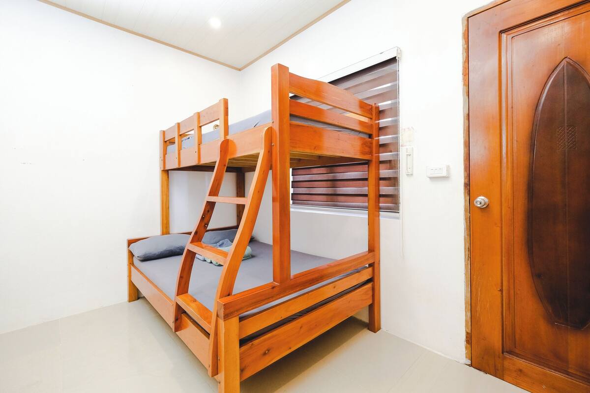 A bunk bed with a ladder, a small table, and a window with blinds.