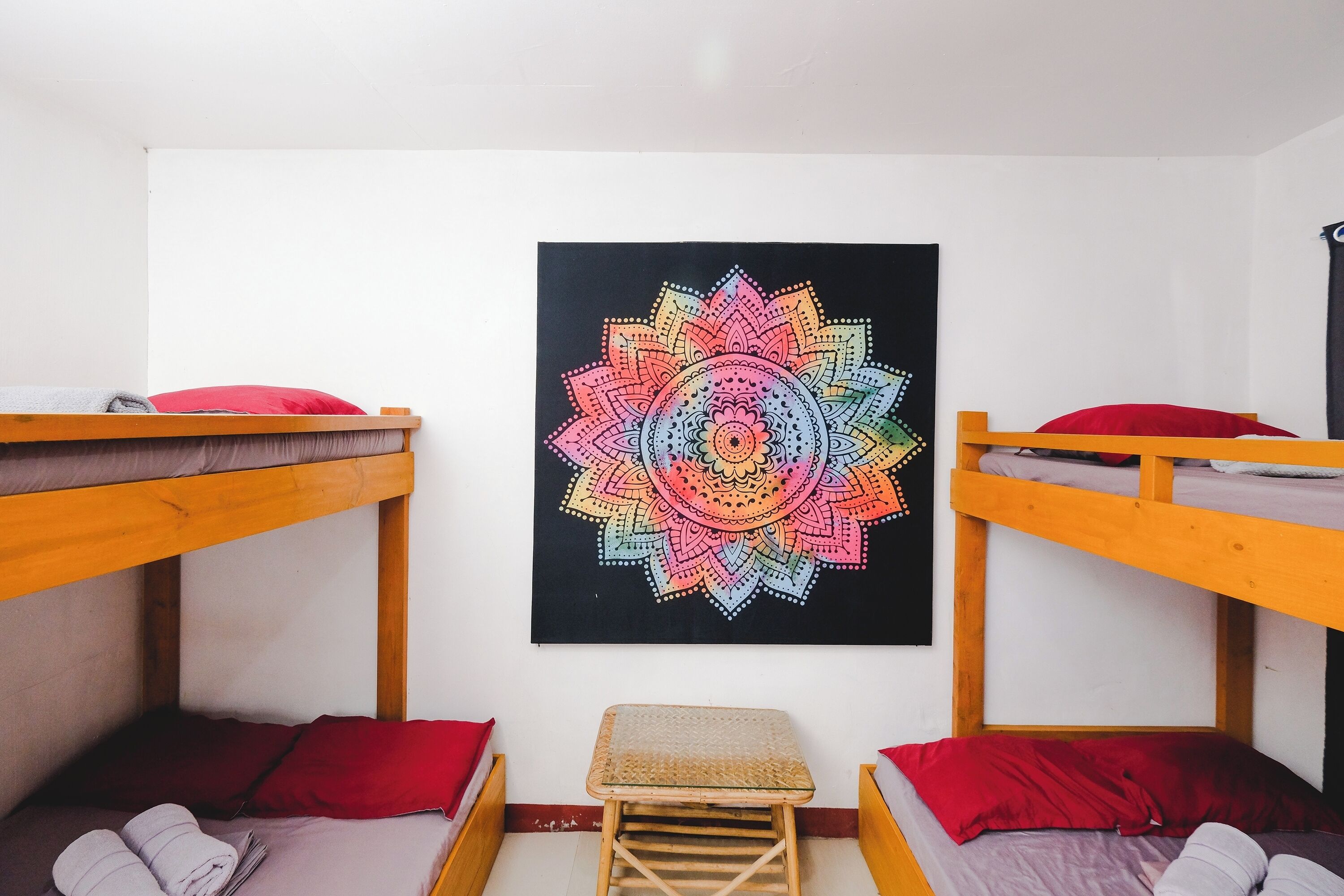 A dormitory room with two bunk beds, a small stool, and a colorful mandala artwork on the wall.