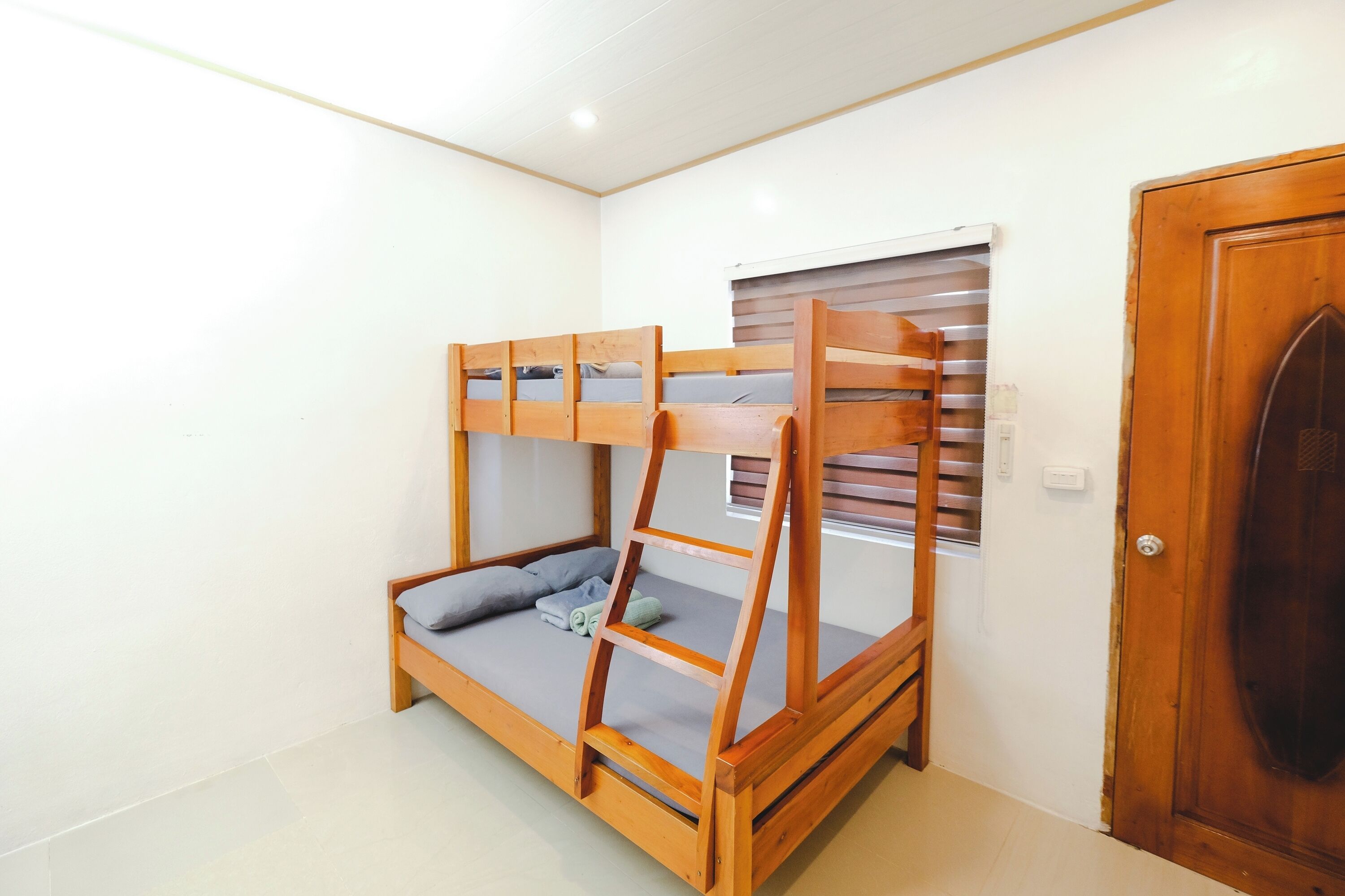 A bunk bed with a wooden frame, a window with blinds, and a wooden door.
