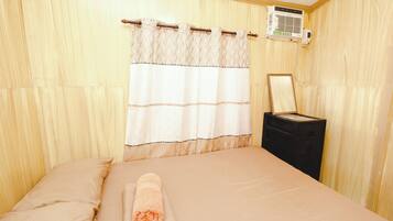 A hotel room with a bed, a towel, a nightstand, a mirror, and an air conditioning unit.