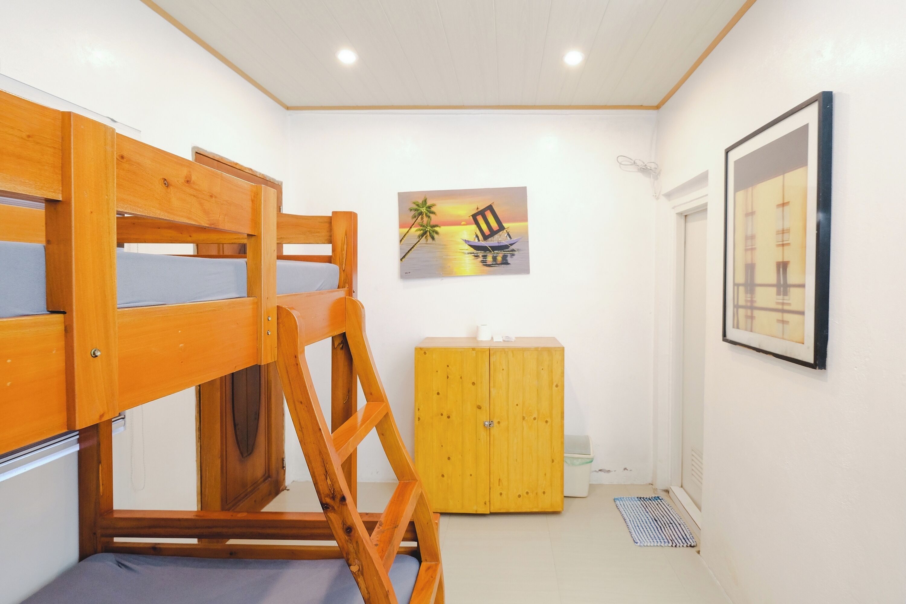 Una cama litera con estructura de madera y un colchón, un armario de madera y un cuadro con una imagen de un atardecer sobre el agua.