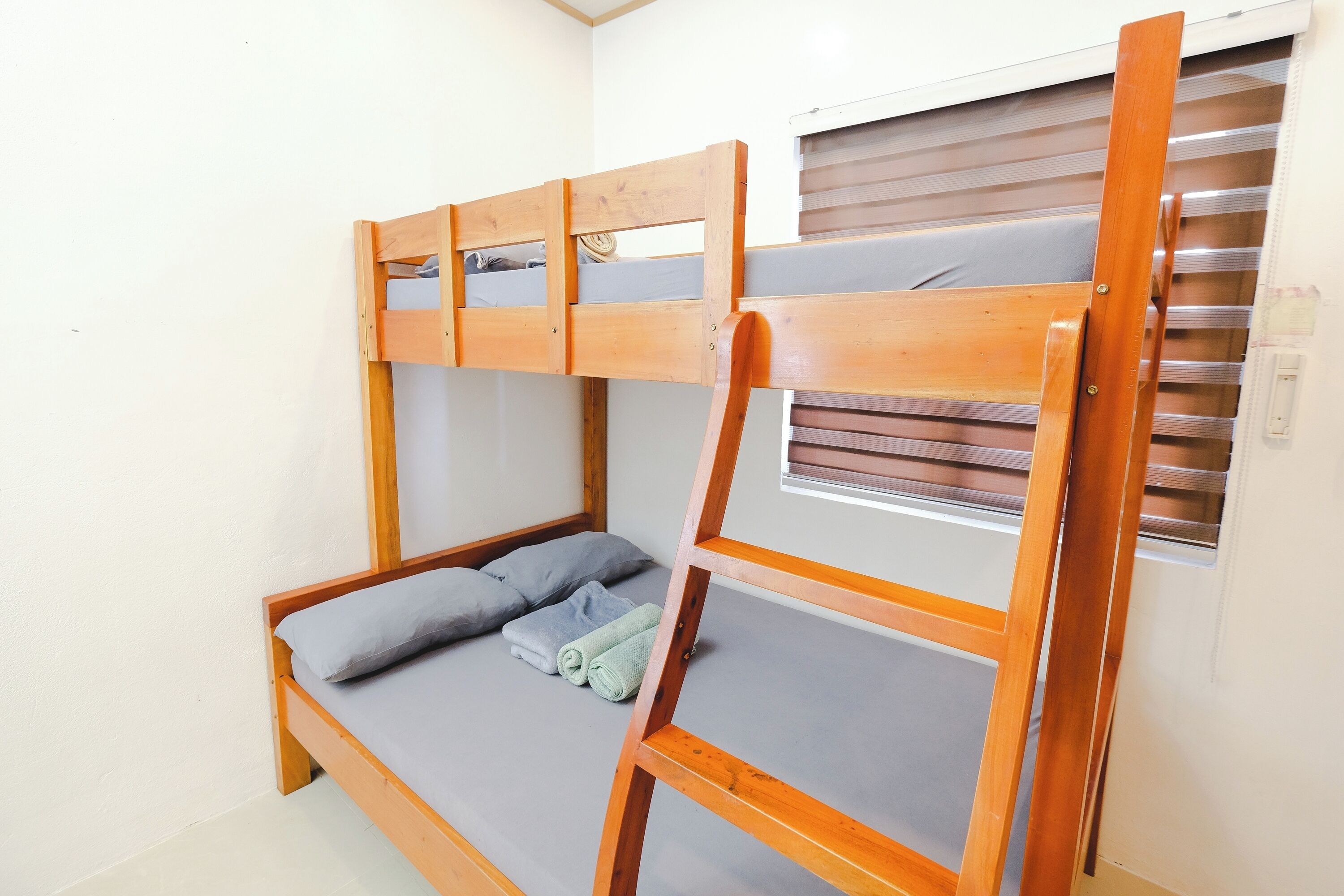 A bunk bed with a wooden frame, a window with blinds, and a small table attached to the bed.