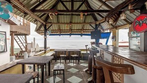 A covered outdoor seating area with tables and chairs, overlooking the sea. - Monaliza Surf Resort (San Juan)