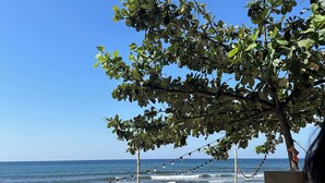 A beach scene with a clear sky, a tree, and beach chairs. - Monaliza Surf Resort (San Juan)