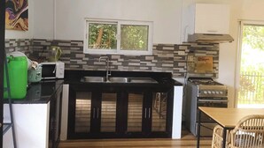 Una cocina compacta con microondas, pileta y estufa. Hay una ventana sobre la pileta y un dispensador de agua verde en la encimera.