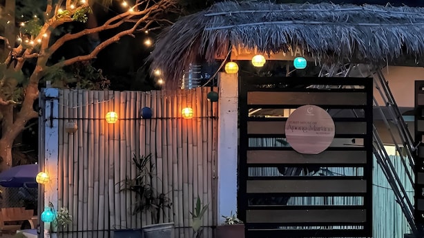 Una entrada protegida con tejado de paja, cerca de bambú y luces colgantes.