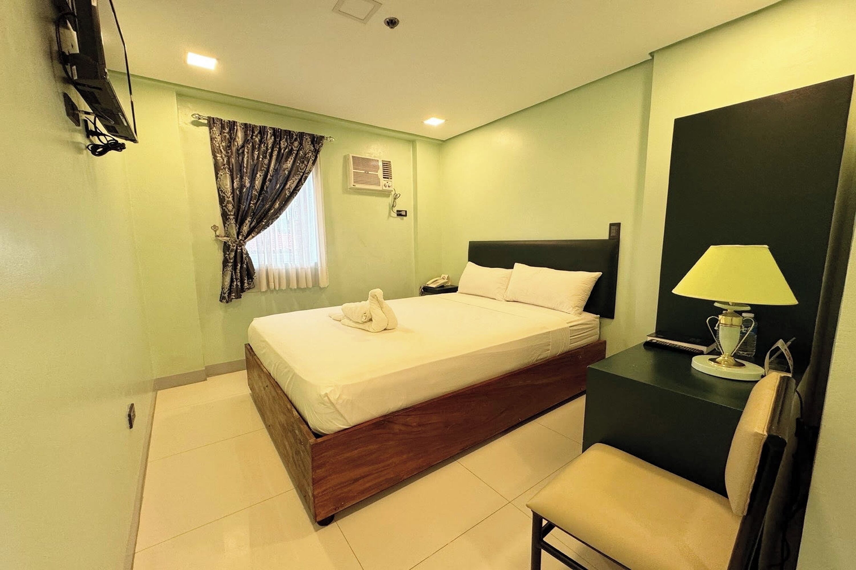 A hotel room with a bed, a desk with a lamp, a chair, a TV, and curtains.