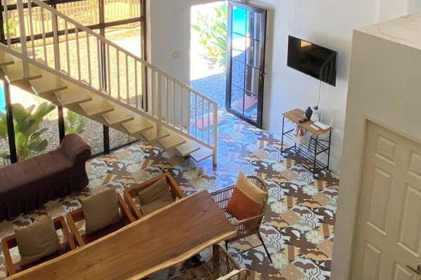 A spacious living area with a wooden table, cushioned seating, a staircase, and a television mounted on the wall. - Casa Calungsod La Union (San Juan)