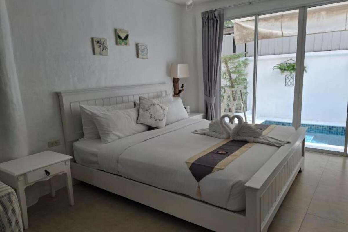 A bedroom with a bed, bedside table, lamp, and a view of the outside.