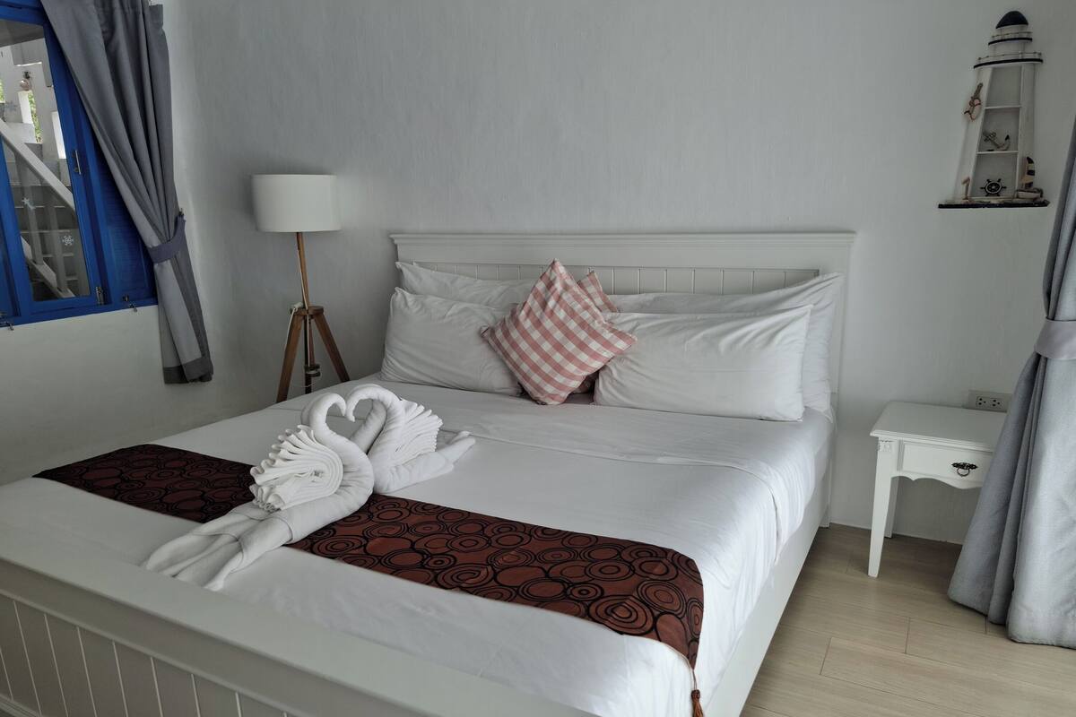 A neatly made bed with white linens, a brown patterned throw, and two swan-shaped towels.