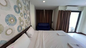 A hotel room with a large bed, a blue chair, and a view of the outside through a window with curtains. - The Nine Place (Hat Yai)