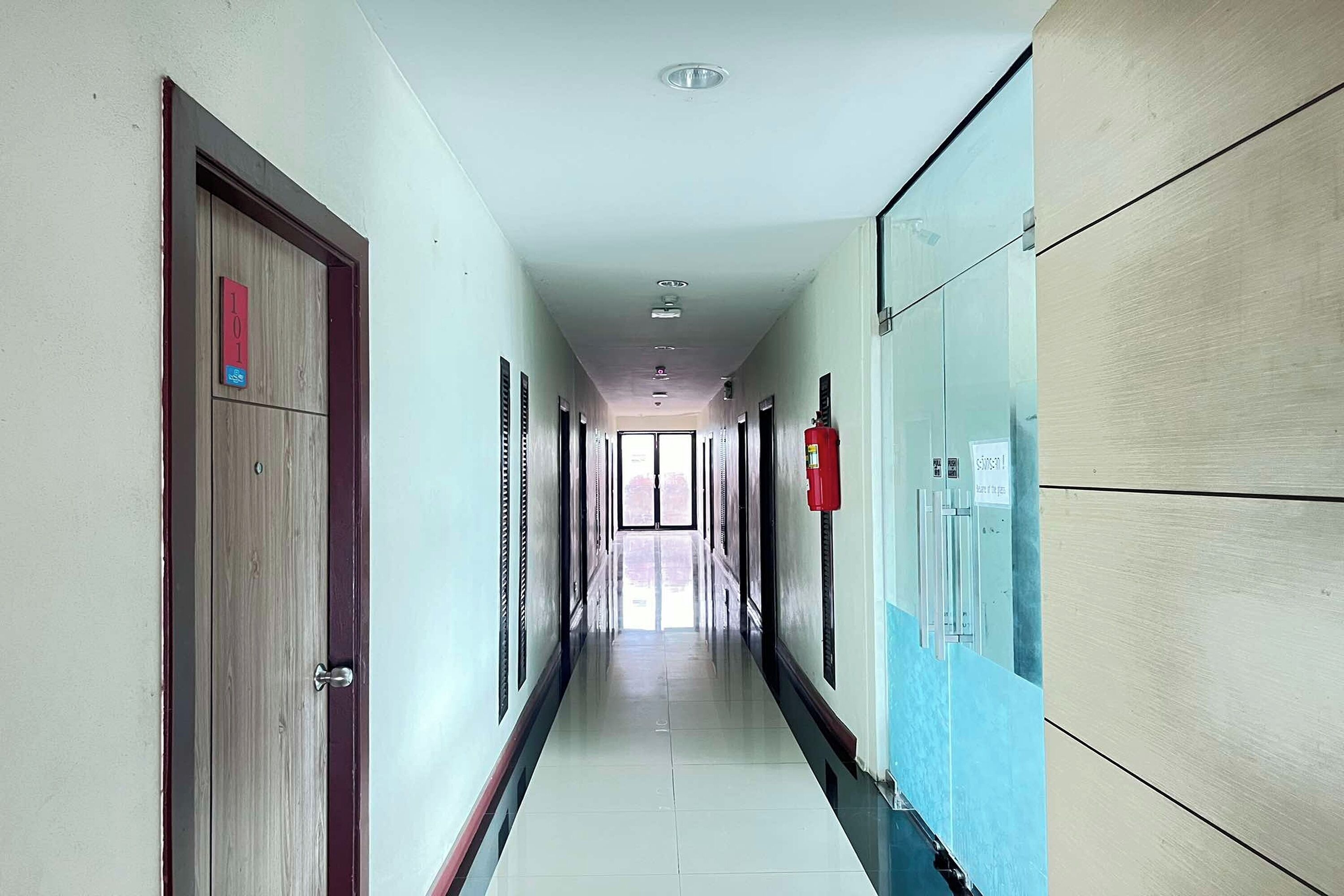 A long, narrow hallway with doors on both sides, a fire extinguisher on the right, and a sign indicating room number 101.