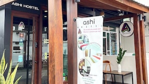 Exterior del ASHI HOSTEL con fachada de madera, un letrero y una planta en maceta.