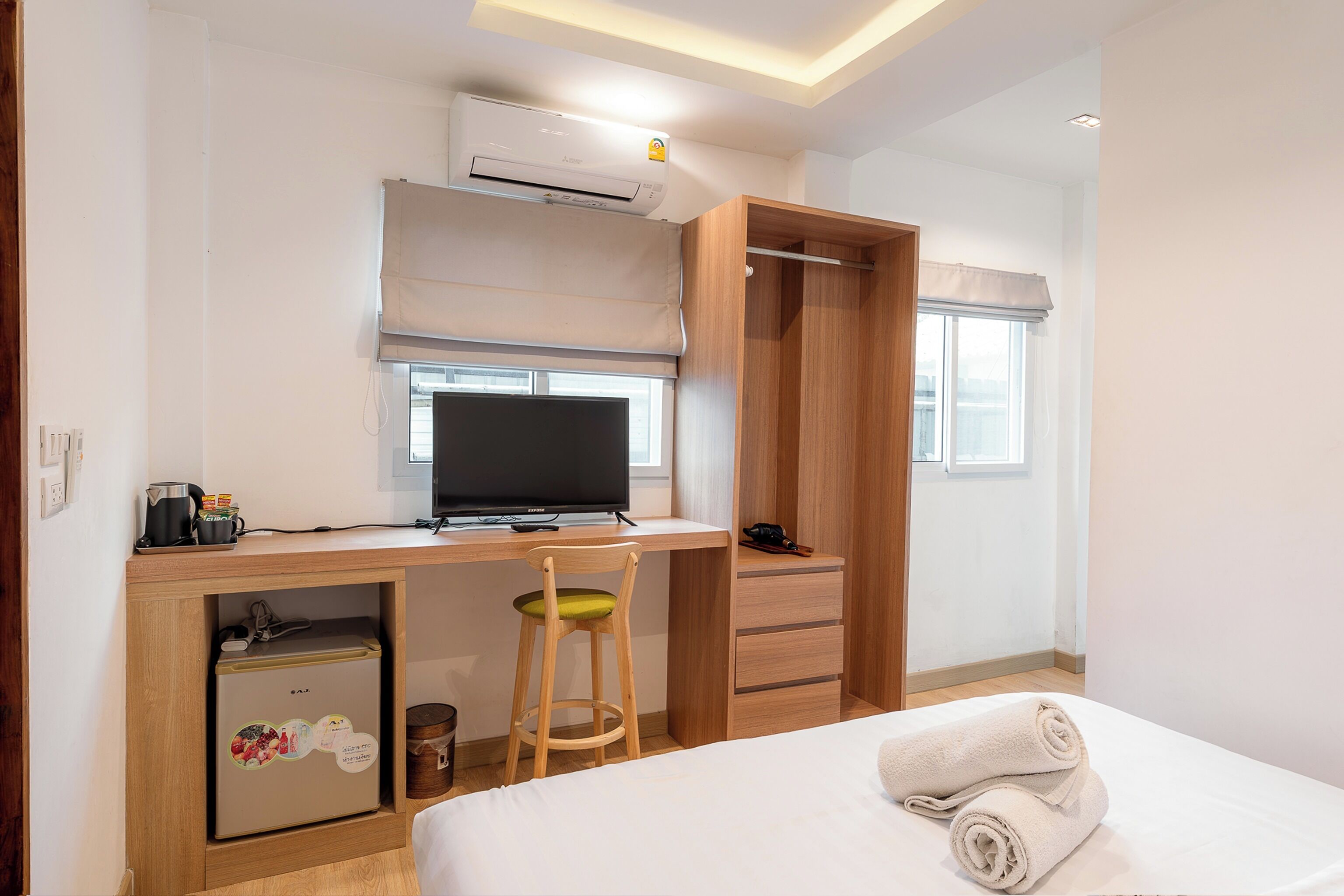 Habitación de hotel con cama, escritorio con computadora, silla, armario y un refrigerador pequeño.