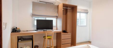 Habitación de hotel con cama, escritorio con computadora, silla, armario y un refrigerador pequeño.