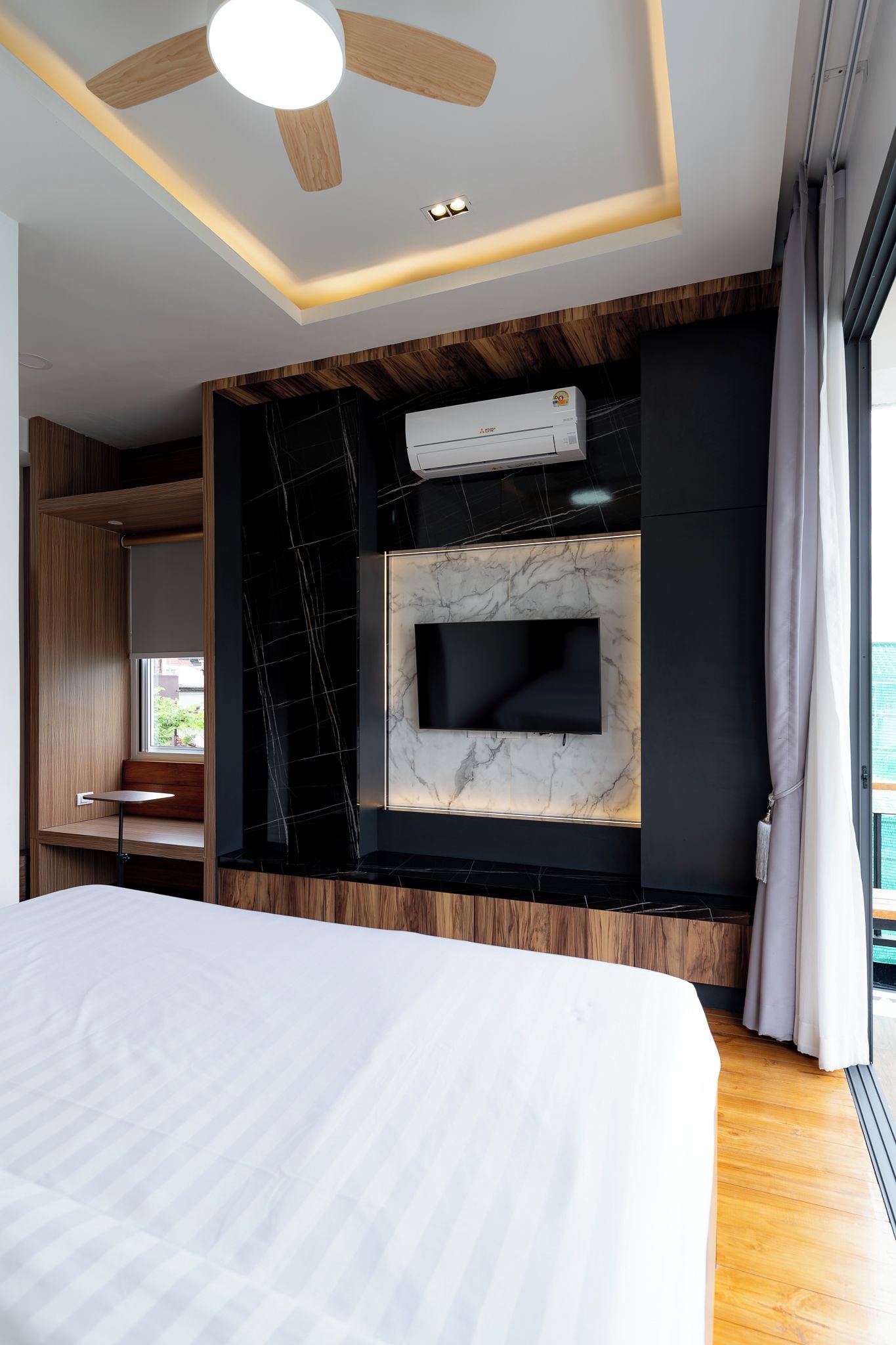 Een moderne hotelkamer met een bed, een plafondventilator, een ingebouwde televisie en een raam met gordijnen.