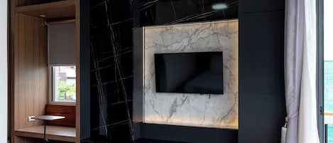 A modern hotel room with a bed, a ceiling fan, a built-in TV, and a window with curtains.