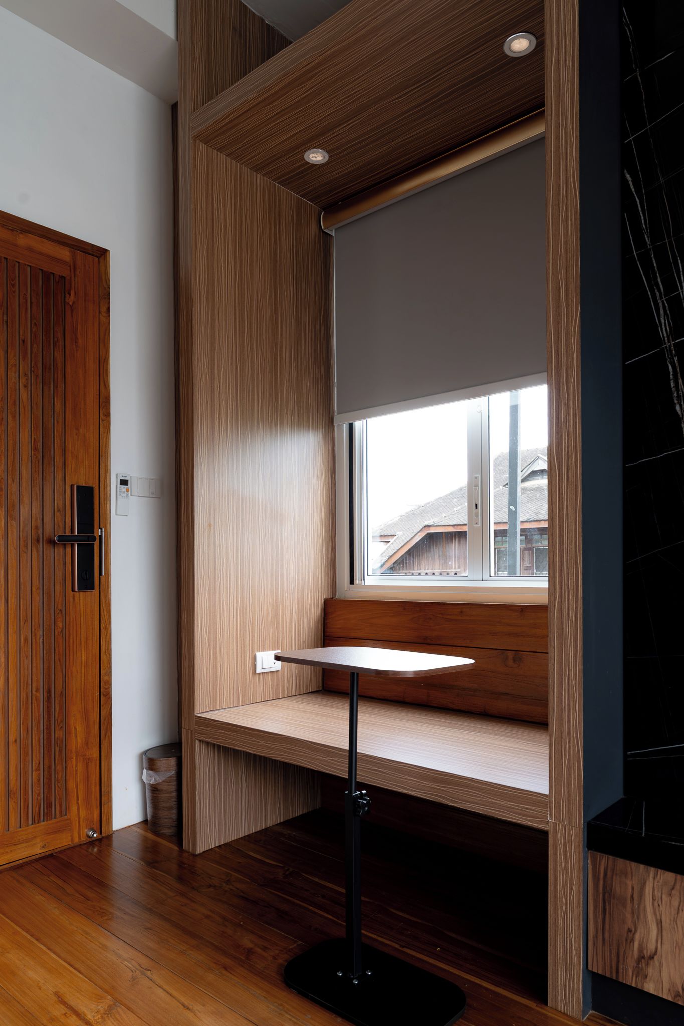 Een moderne kamer met een ingebouwde bank bij een raam, een houten deur en een plafond met inbouwspots.