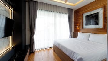 Una habitación de hotel con cama, televisor, paneles de madera y un amplio ventanal con cortinas.