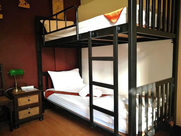 Habitación con literas, una lámpara de escritorio verde, una mesita de noche de madera y una manta roja.