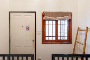 A room with a white door, a window with a wooden frame and a beige curtain, and a wooden ladder leaning against the wall. - Ashi Poshtel (Chiang Mai)