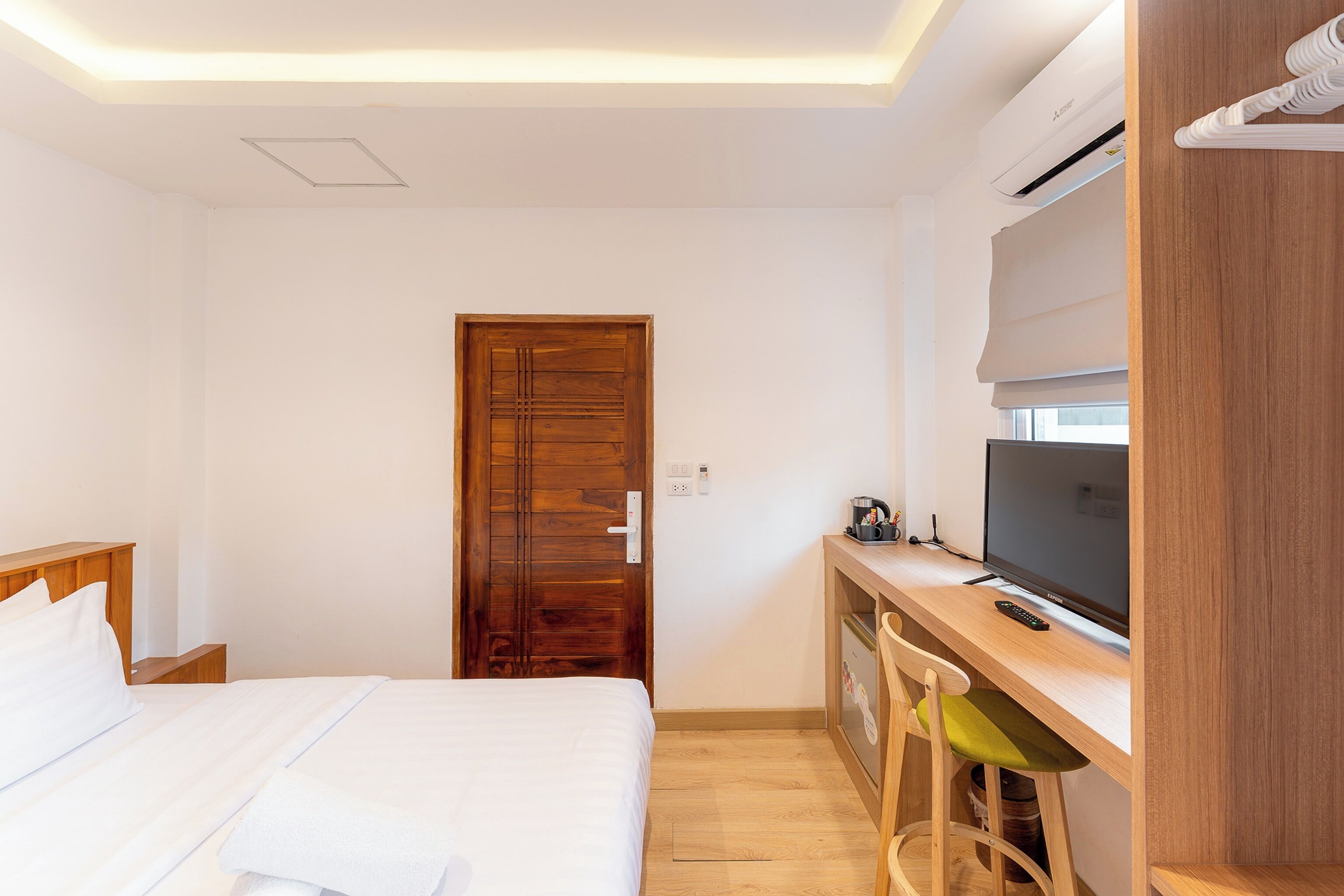 Une chambre d’hôtel avec un lit, un bureau avec une télévision, une chaise et une porte en bois.