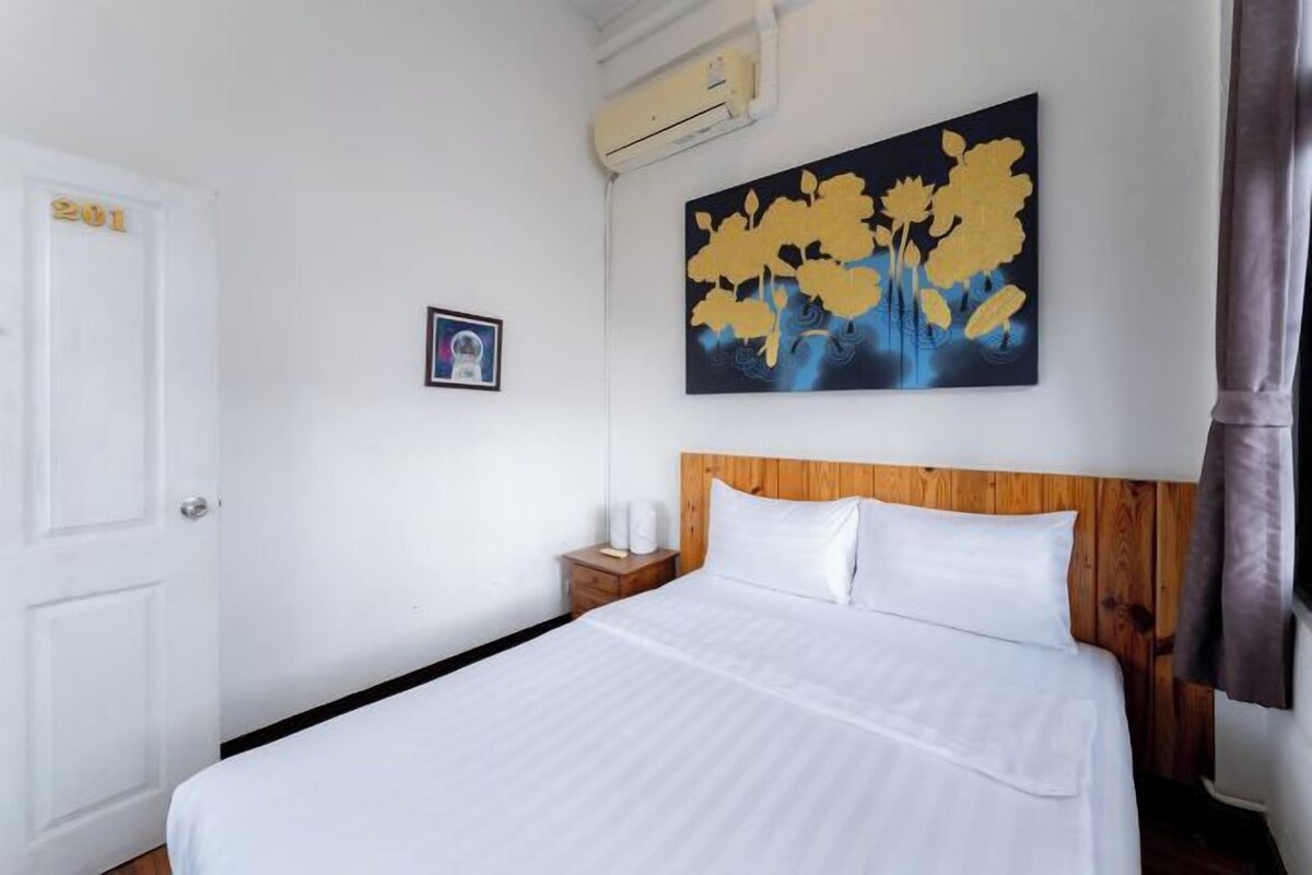 Habitación de hotel con cama, cabecera de madera, mesita de noche, aire acondicionado montado en la pared y un cuadro.
