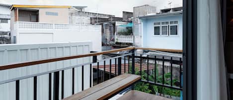 A balcony with a wooden floor, a bench, and a view of neighboring buildings.