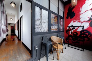 A hallway with a wooden floor, a black-framed door with a window, and a red mural on the wall. - Ashi Poshtel (Chiang Mai)