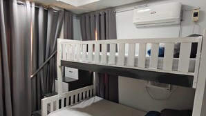 A bunk bed with a white headboard, a bedside table with a lamp, and a wall-mounted air conditioner. - Ada's Residential Villa La Union (Bacnotan)