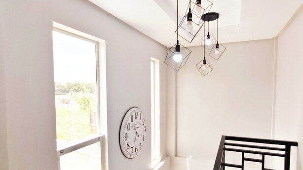 A room with a large window, a wall clock, and a hanging light fixture. - Ada's Residential Villa La Union (Bacnotan)