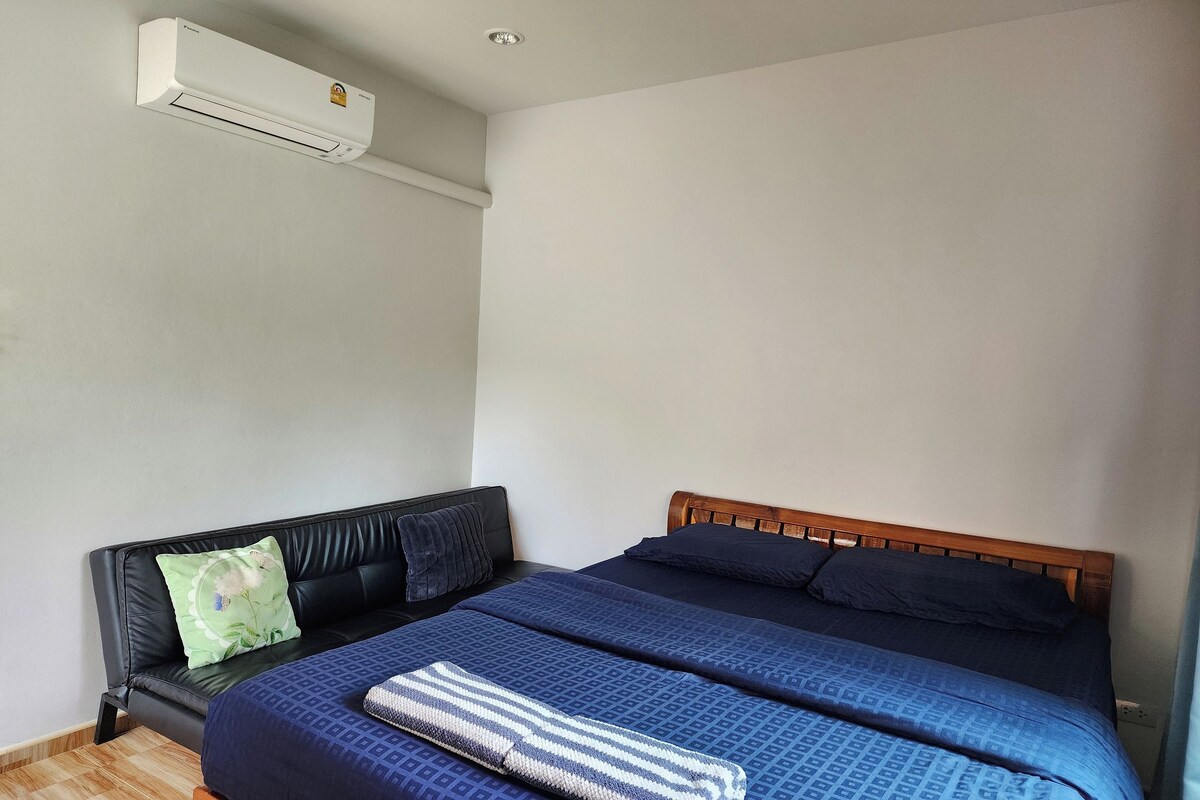 A bedroom with a bed, a black leather sofa, and a wall-mounted air conditioner.