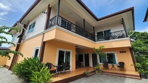A two-story building with a balcony on the upper floor, a covered entrance, and a paved patio area with outdoor seating. - 99 House (Pattaya)