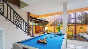 A pool table in a room with a staircase and a slide in the background. - 99 Pool Villa (Pattaya)