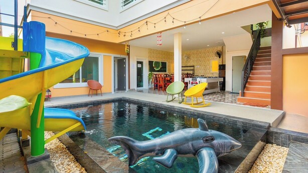 An indoor swimming pool with a dolphin sculpture, a colorful slide, and a staircase leading to an upper level. - 99 Pool Villa (Pattaya)