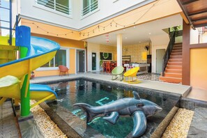 An indoor swimming pool with a dolphin sculpture, a colorful slide, and a staircase leading to an upper level. - 99 Pool Villa (Pattaya)
