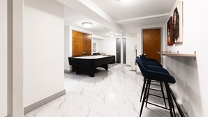 Un interior moderno con mesa de billar, una zona de bar con taburetes y un comedor.