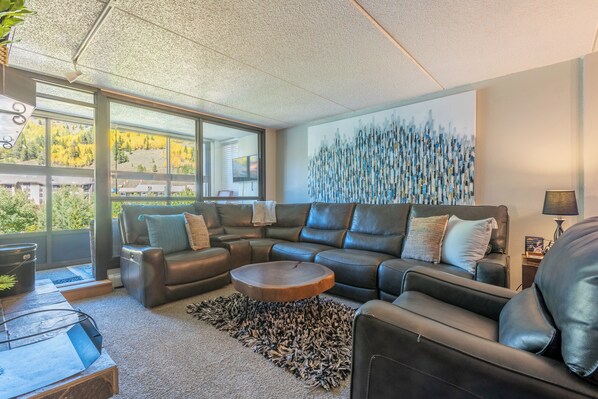 A modern living room with a leather sofa, a round coffee table, and a large abstract painting on the wall.