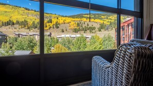 A room with a large window offering a view of a hillside with yellow foliage, a red building, and several residential structures. - Mountain Plaza 310  1 BD/ 2 BA (Copper Mountain)