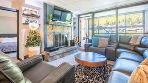 A modern living room with a fireplace, leather sofas, and a large window offering a view of the outdoors. - Mountain Plaza 310  1 BD/ 2 BA (Copper Mountain)