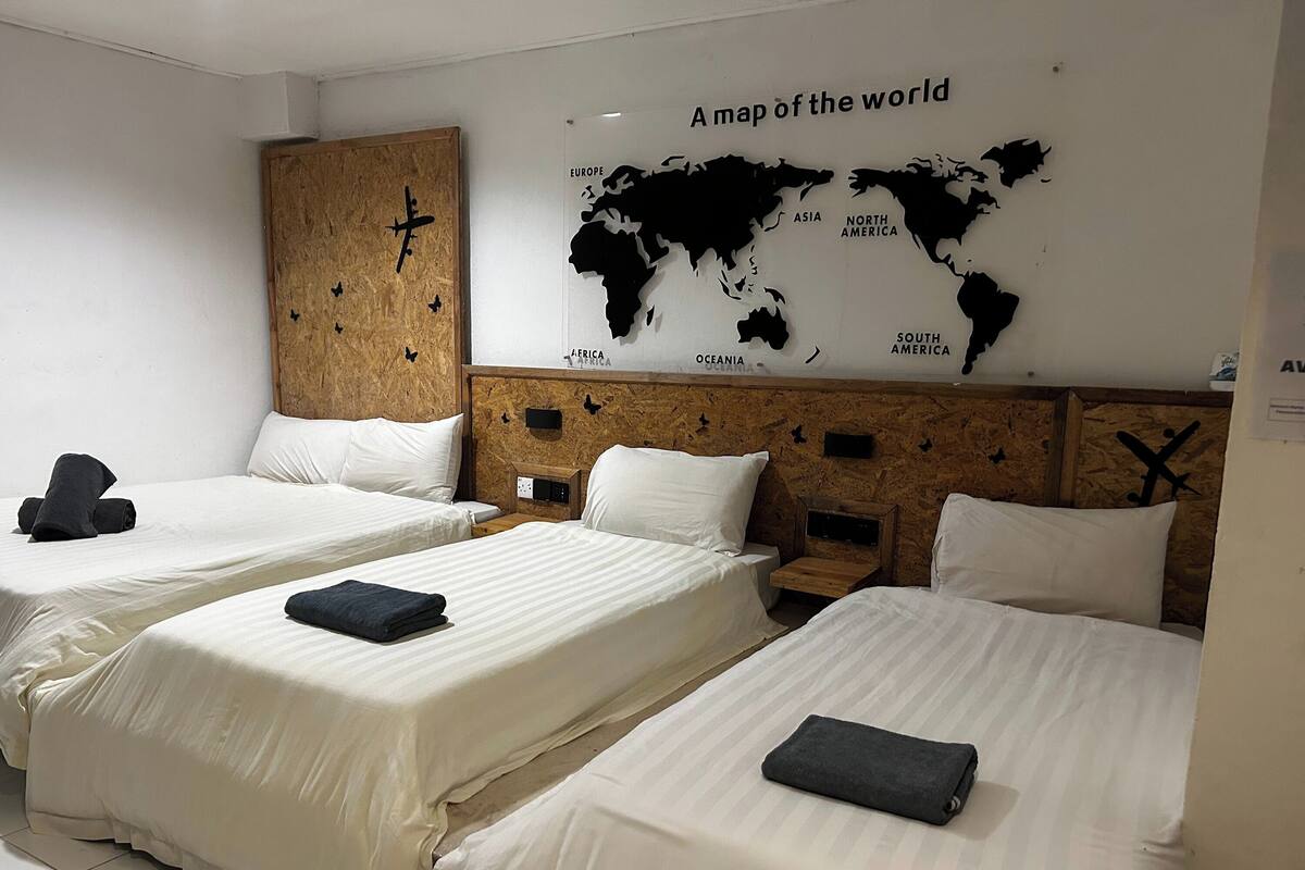 A hotel room with two beds, a wooden headboard, a world map on the wall, and a wooden shelf with a cross.