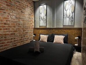A room with a brick wall, a bed with black and pink pillows, and a wooden headboard.
