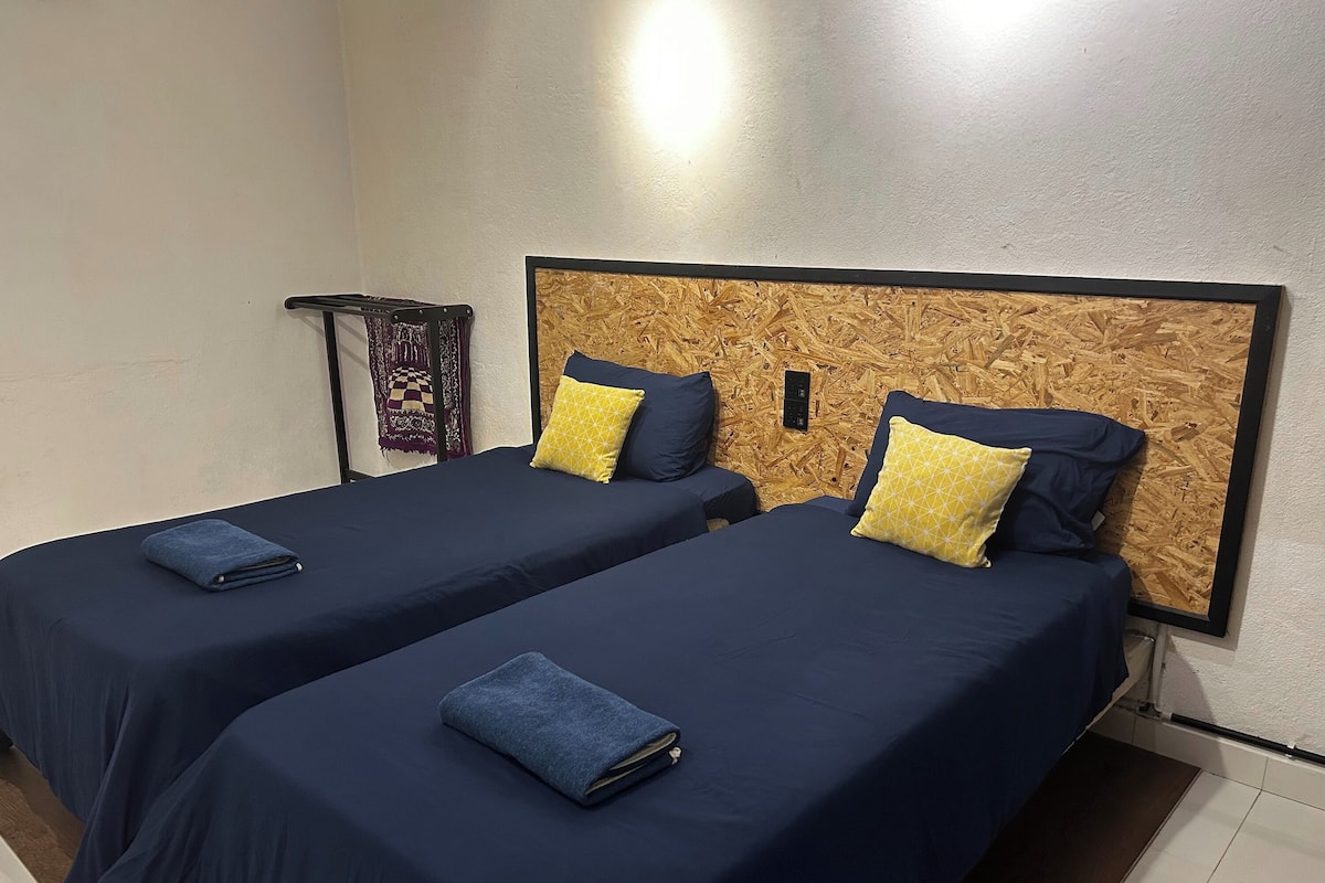 A hotel room with two beds, each with navy blue bedding and decorative pillows.