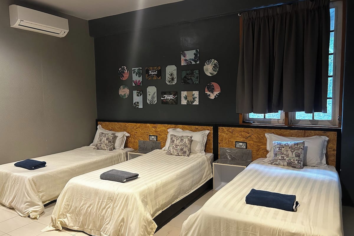 A hotel room with three beds, a wall-mounted air conditioner, and a window with curtains.