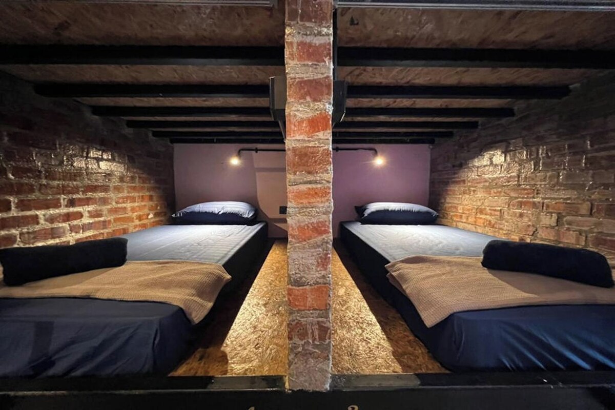 A room with two beds, a brick pillar, exposed beams, and a purple wall.